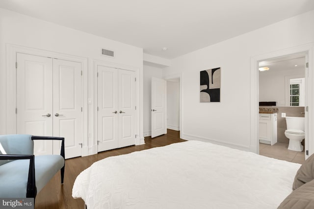 bedroom featuring ensuite bathroom, two closets, and dark hardwood / wood-style flooring