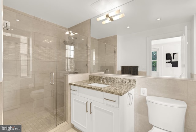 bathroom with tile walls, vanity, toilet, and a shower with door