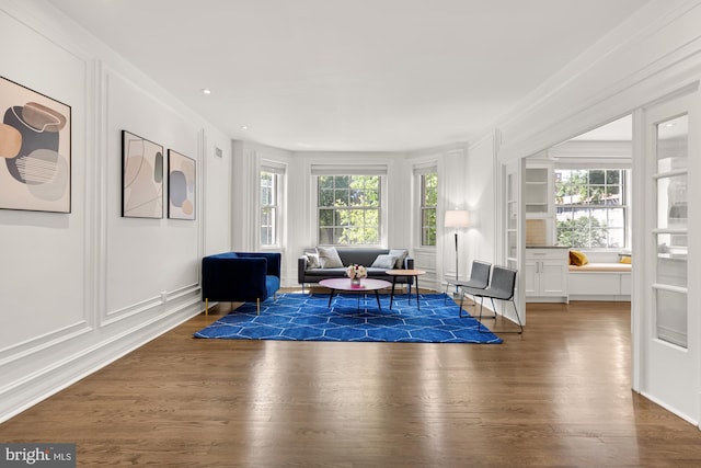 living area featuring dark wood-type flooring, a healthy amount of sunlight, and crown molding