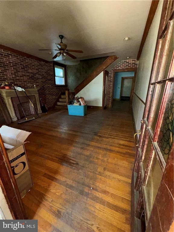 unfurnished living room with brick wall, ceiling fan, and wood-type flooring