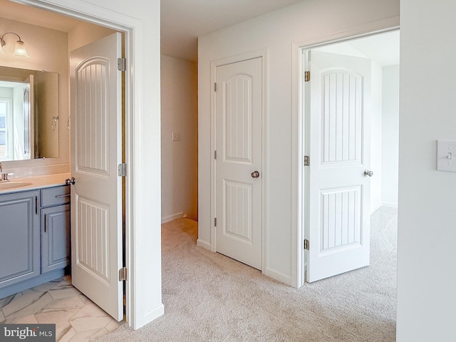 corridor featuring light colored carpet, baseboards, marble finish floor, and a sink