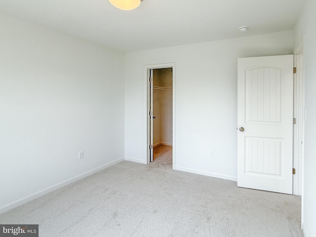 unfurnished bedroom with a closet, carpet flooring, a walk in closet, and baseboards