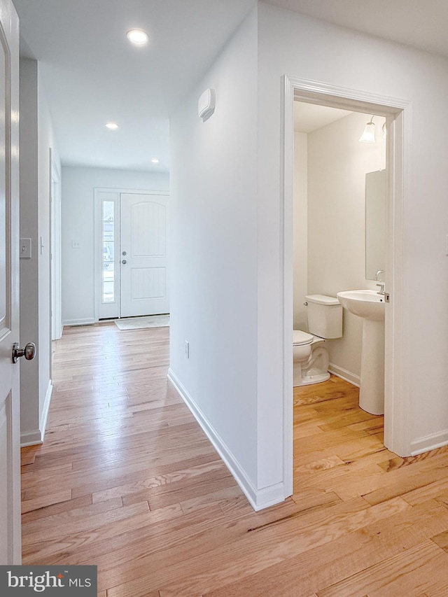 hall featuring recessed lighting, baseboards, a sink, and light wood finished floors