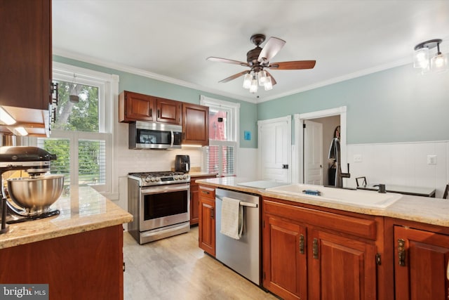 kitchen with light wood-type flooring, crown molding, sink, ceiling fan, and appliances with stainless steel finishes