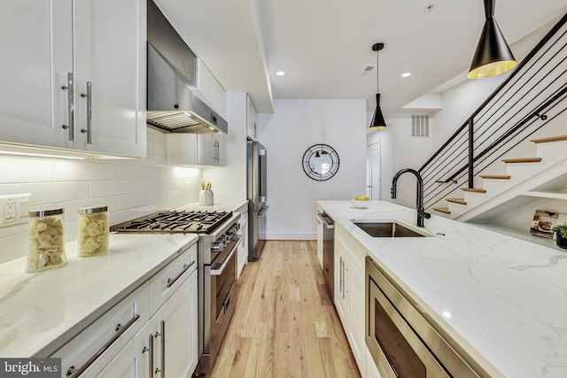 kitchen with pendant lighting, sink, white cabinetry, wall chimney range hood, and stainless steel appliances