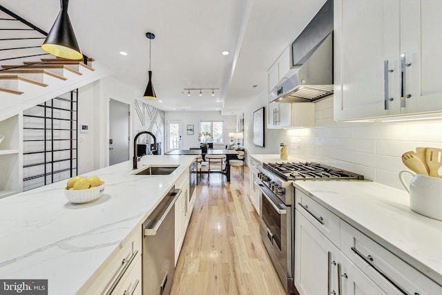 kitchen featuring white cabinets, hanging light fixtures, sink, light hardwood / wood-style flooring, and appliances with stainless steel finishes