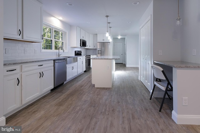 kitchen with a kitchen island, decorative light fixtures, light hardwood / wood-style flooring, white cabinetry, and appliances with stainless steel finishes