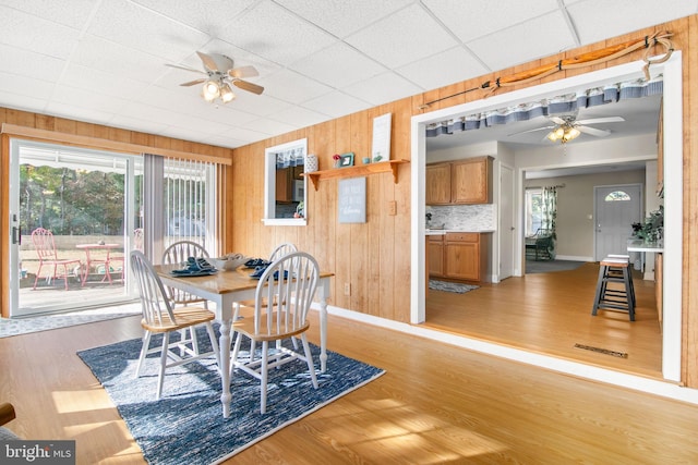 dining room with hardwood / wood-style floors, a drop ceiling, ceiling fan, and wood walls