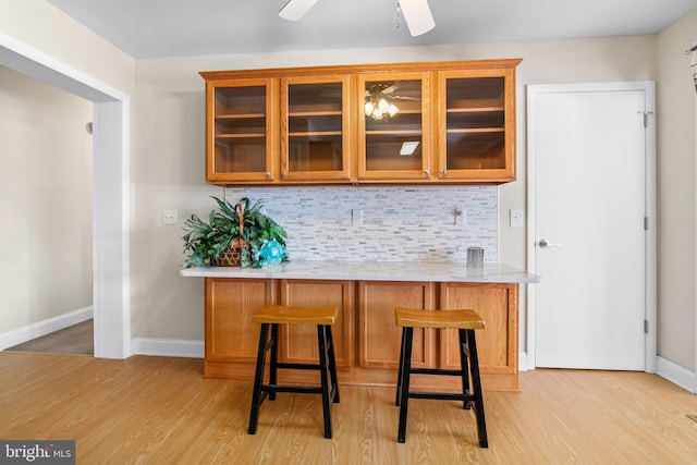 bar with light hardwood / wood-style flooring, backsplash, and ceiling fan