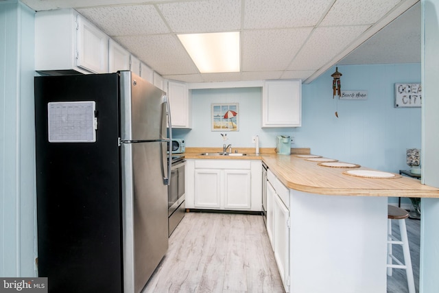 kitchen featuring appliances with stainless steel finishes, light hardwood / wood-style floors, white cabinets, kitchen peninsula, and a breakfast bar area