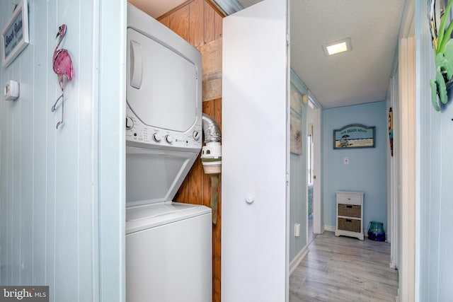 clothes washing area with a textured ceiling, stacked washer and dryer, and light hardwood / wood-style flooring