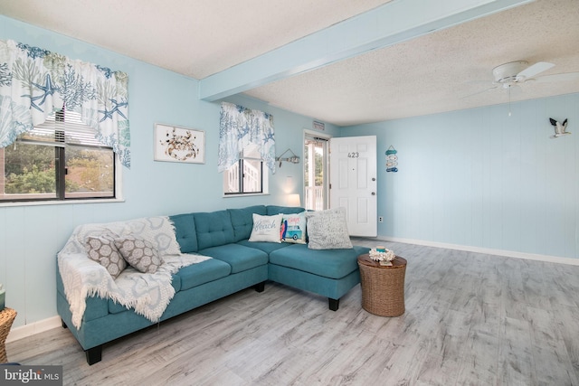 living room featuring light hardwood / wood-style flooring, beam ceiling, ceiling fan, and a textured ceiling