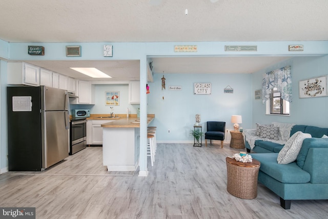 kitchen featuring light hardwood / wood-style floors, a breakfast bar area, white cabinetry, kitchen peninsula, and stainless steel appliances