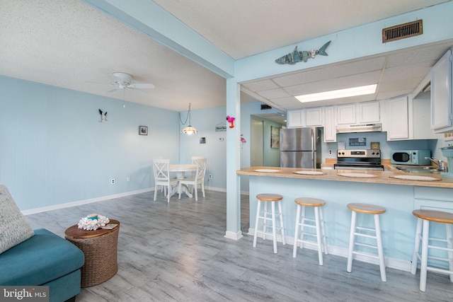 kitchen featuring white cabinets, kitchen peninsula, appliances with stainless steel finishes, light wood-type flooring, and a kitchen bar