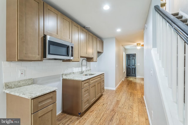 kitchen featuring tasteful backsplash, sink, light wood-type flooring, ceiling fan, and light stone counters