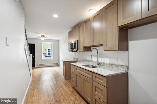 kitchen featuring a baseboard heating unit, backsplash, sink, light wood-type flooring, and light stone counters