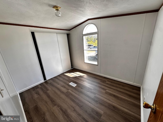 unfurnished bedroom with a textured ceiling, vaulted ceiling, a closet, dark wood-type flooring, and ornamental molding