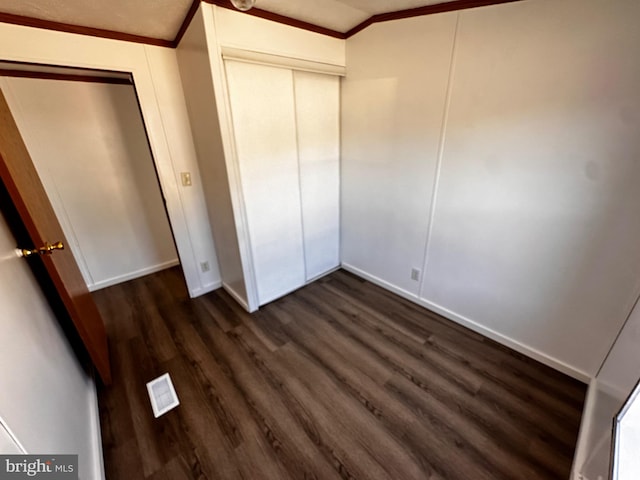 unfurnished bedroom with lofted ceiling, crown molding, dark hardwood / wood-style floors, and a closet