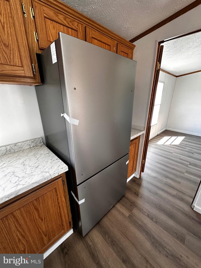 kitchen with crown molding, dark hardwood / wood-style flooring, stainless steel refrigerator, and a textured ceiling