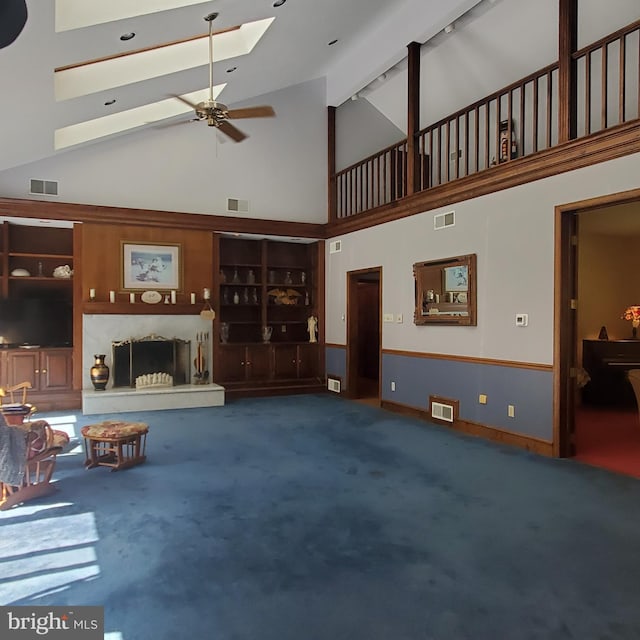 carpeted living room with ceiling fan, a skylight, beam ceiling, a high end fireplace, and high vaulted ceiling