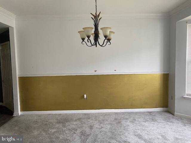 empty room with carpet, a notable chandelier, and ornamental molding