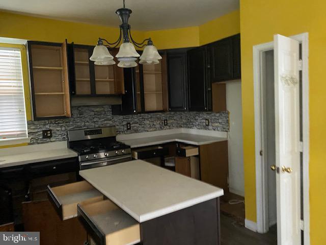 kitchen featuring backsplash, an inviting chandelier, stainless steel gas stove, decorative light fixtures, and a kitchen island