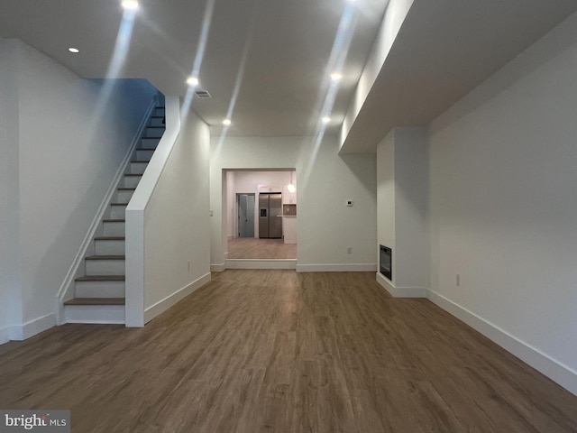 unfurnished living room featuring visible vents, baseboards, wood finished floors, and stairs