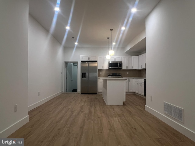 kitchen with hanging light fixtures, white cabinets, appliances with stainless steel finishes, hardwood / wood-style flooring, and a center island