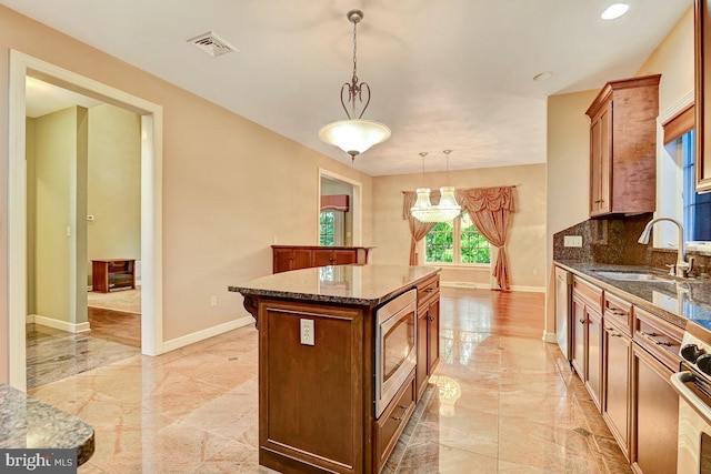 kitchen with sink, a kitchen island, decorative light fixtures, appliances with stainless steel finishes, and decorative backsplash