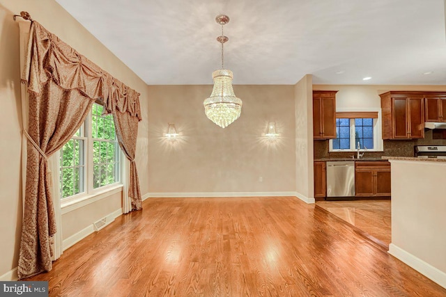 kitchen with decorative backsplash, stainless steel appliances, light hardwood / wood-style flooring, decorative light fixtures, and a chandelier