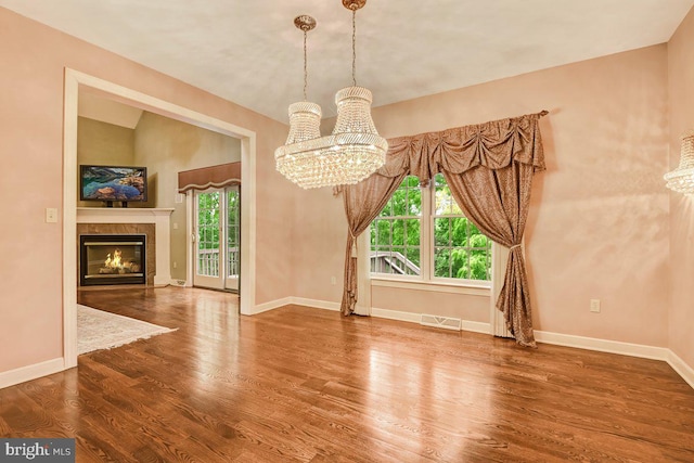 unfurnished dining area featuring an inviting chandelier, hardwood / wood-style flooring, a tiled fireplace, and vaulted ceiling