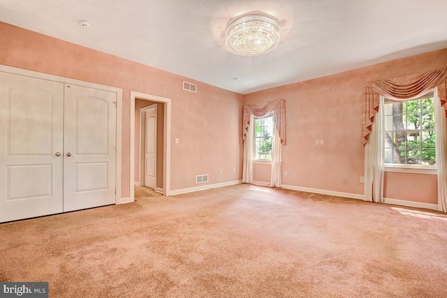 unfurnished bedroom with multiple windows, a closet, light colored carpet, and a notable chandelier