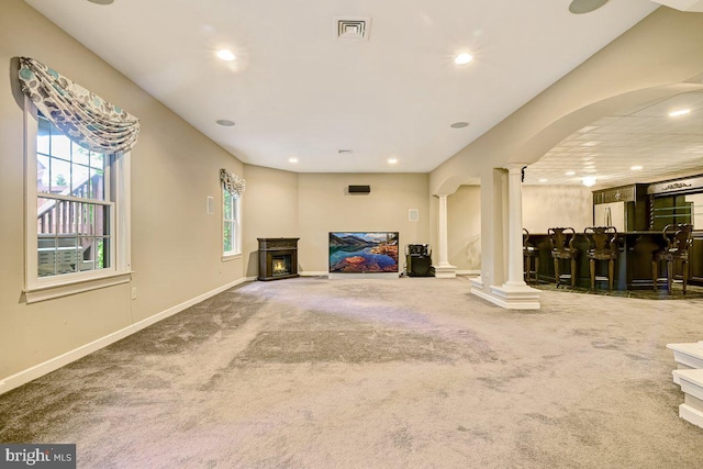 unfurnished living room with bar area, ornate columns, and carpet