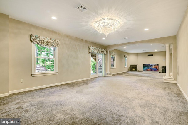 unfurnished living room featuring a healthy amount of sunlight, decorative columns, and light colored carpet