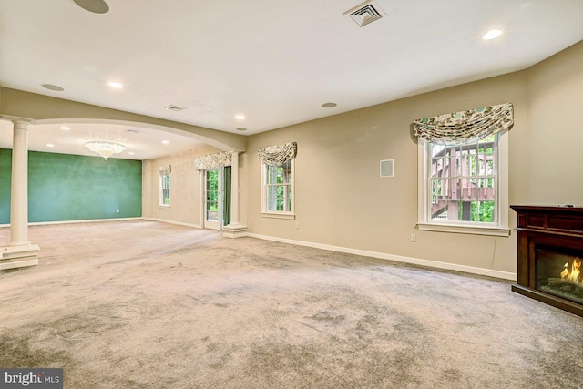 unfurnished living room featuring ornate columns, carpet flooring, and plenty of natural light