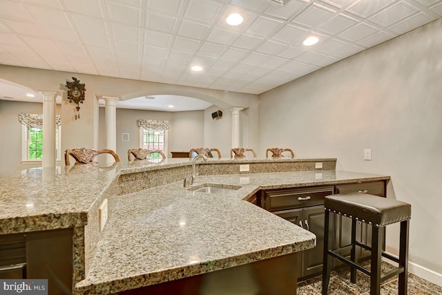 kitchen featuring dark brown cabinets, decorative columns, sink, and light stone counters