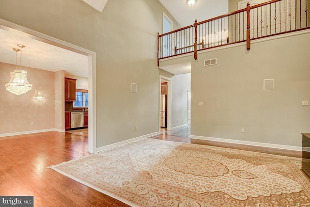 unfurnished living room with high vaulted ceiling, a chandelier, and hardwood / wood-style flooring