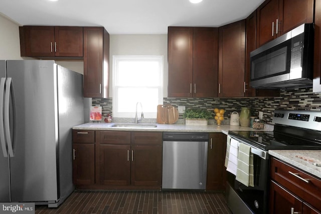 kitchen featuring stainless steel appliances, dark brown cabinetry, sink, light stone counters, and tasteful backsplash