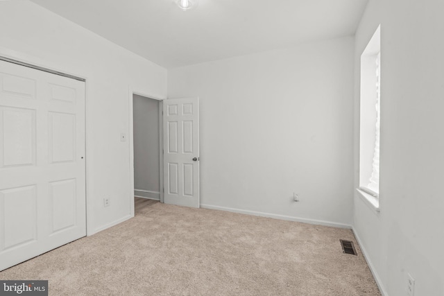 unfurnished bedroom with light colored carpet and a closet