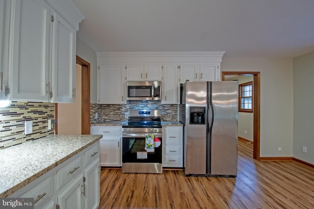 kitchen featuring decorative backsplash, white cabinets, light stone countertops, stainless steel appliances, and light hardwood / wood-style flooring