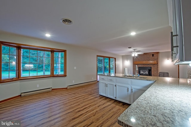 kitchen with ceiling fan, a brick fireplace, plenty of natural light, white cabinetry, and a baseboard radiator