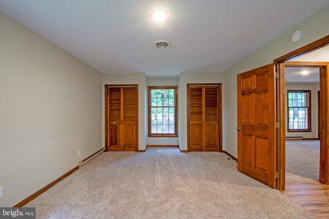 unfurnished bedroom with a baseboard heating unit and light colored carpet