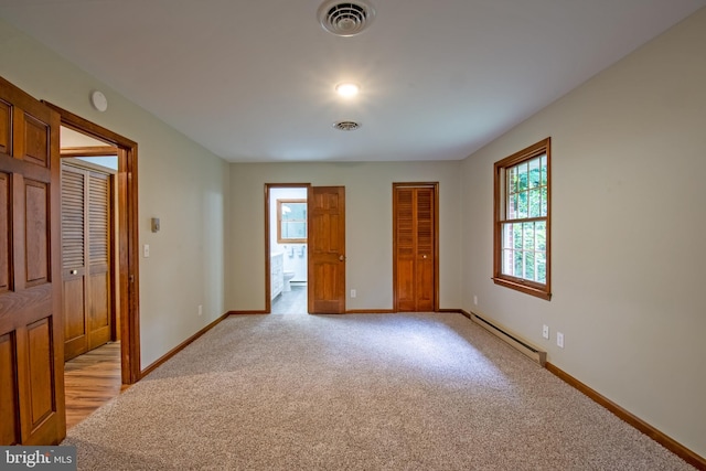 spare room featuring light colored carpet, baseboard heating, and plenty of natural light