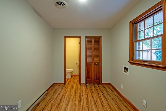 unfurnished bedroom featuring a closet, light hardwood / wood-style flooring, ensuite bathroom, and a baseboard radiator