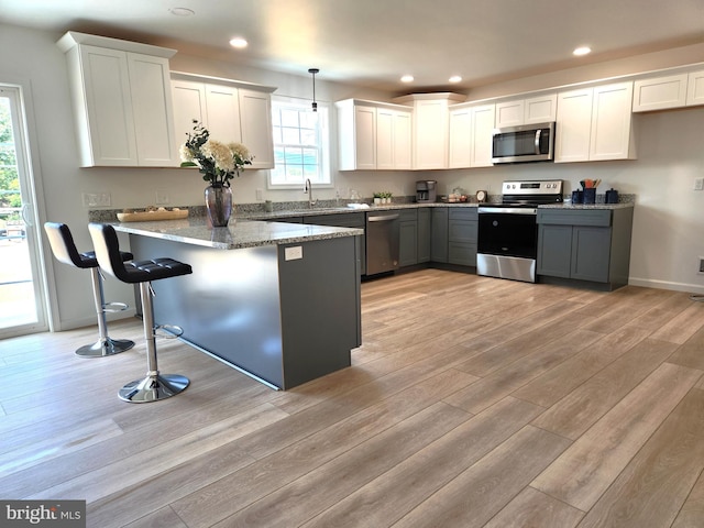 kitchen with stainless steel appliances, white cabinetry, and decorative light fixtures