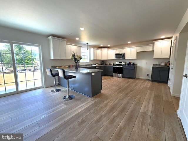 kitchen featuring appliances with stainless steel finishes, kitchen peninsula, white cabinetry, and light hardwood / wood-style flooring