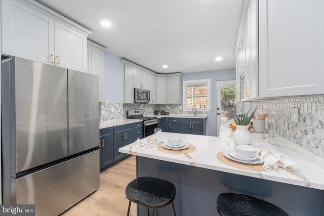 kitchen with a breakfast bar, sink, white cabinets, stainless steel appliances, and blue cabinets