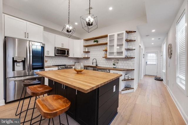 kitchen with appliances with stainless steel finishes, wooden counters, a kitchen island, and a healthy amount of sunlight