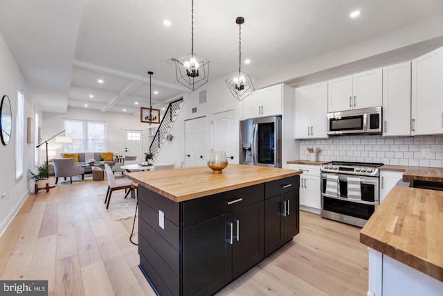 kitchen featuring light hardwood / wood-style flooring, butcher block counters, stainless steel appliances, hanging light fixtures, and white cabinets