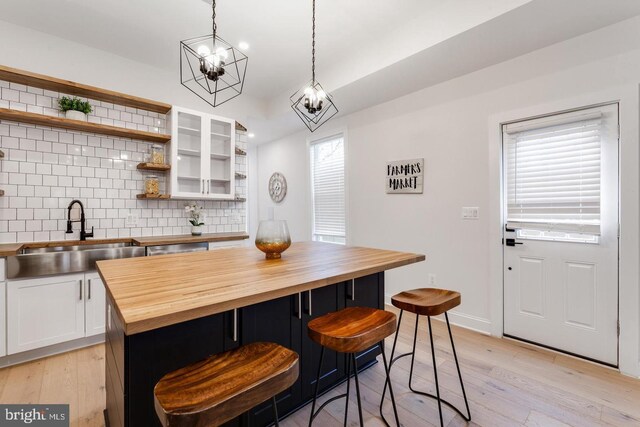 kitchen with white cabinets, an inviting chandelier, sink, a kitchen breakfast bar, and butcher block counters